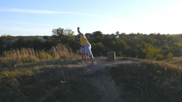 Ung sportig man står vid yogaställning utomhus. Kaukasiska kille öva yoga flyttar och positioner i naturen. Idrottsman balansering. Vackert landskap som bakgrund. Hälsosam aktiv livsstil — Stockvideo