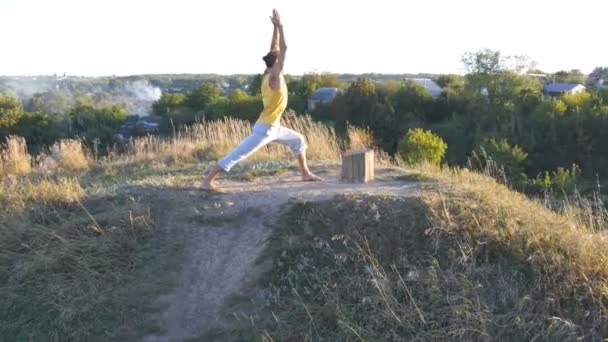 Sportieve jongeman permanent op yoga pose buiten. Kaukasische guy beoefenen van yoga beweegt en posities in de natuur. Mooi landschap als achtergrond. Gezonde actieve levensstijl — Stockvideo