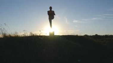 Yogi Yoga uygulamak hareket eder ve doğal olarak konumlandırır. Sportif adam poz yoga açık ayakta silüeti. Tek ayak üstünde Dengeleme atlet. Güzel gökyüzü ve güneş arka plan olarak. Sağlıklı aktif yaşam tarzı