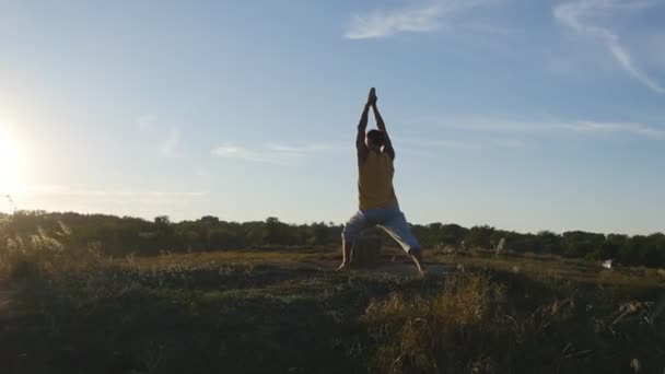 Joven deportista de pie en yoga posan al aire libre. Hombre caucásico practicando movimientos de yoga y posiciones en la naturaleza. Atleta balanceándose. Hermoso paisaje como fondo. Vida activa saludable — Vídeo de stock
