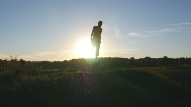 Silhuett av sportig man som stående hos yogaposer utomhus. Yogi utövar yogarörelser och positioner i naturen. Idrottare balanserar på ett ben. Vacker himmel och sol som bakgrund. Hälsosam aktiv livsstil — Stockvideo