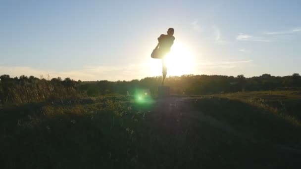 ヨギのヨガの練習は、移動し、自然の中の位置します。屋外ヨガのポーズで立っているスポーティな男のシルエット。片足でバランス運動選手。美しい空と太陽の背景として。健康的なアクティブなライフ スタイル — ストック動画