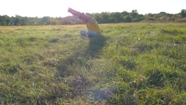 Joven sentado en la hierba verde en el prado y haciendo ejercicio de yoga. Tipo musculoso estirando su cuerpo en la naturaleza. Entrenamiento al aire libre en un día soleado. Hermoso paisaje de fondo. De cerca. — Vídeos de Stock