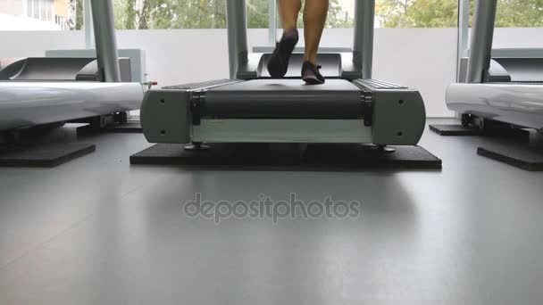 Piernas femeninas caminando en la cinta en el gimnasio. Mujer joven haciendo ejercicio durante el ejercicio cardiovascular. Los pies de las niñas en zapatos deportivos de entrenamiento en interiores en el club deportivo. De cerca. — Vídeos de Stock