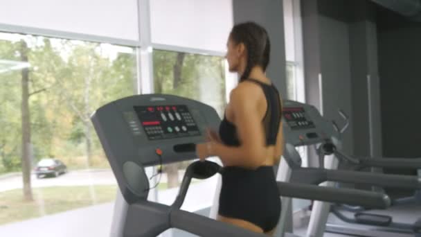 Mujer joven y fuerte con cuerpo de fitness perfecto en ropa deportiva corriendo en la cinta de correr en el gimnasio. Chica haciendo ejercicio durante el ejercicio cardiovascular. Entrenamiento femenino en interior en el club deportivo. Gente corriendo. De cerca. — Vídeo de stock