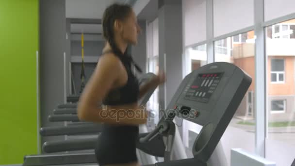 Jovem mulher forte com corpo de fitness perfeito em sportswear correndo em esteira rolante no ginásio. Exercício da menina durante o exercício cardio. Treinamento feminino indoor no clube esportivo. Pessoas a correr. Fechar — Vídeo de Stock