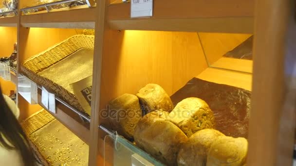 Mulher escolhe e colocar um pão fresco em um pacote no supermercado. Menina pegando um pedaço de pão da prateleira, cheirando-o e colocando-o no cesto. Compras na mercearia — Vídeo de Stock