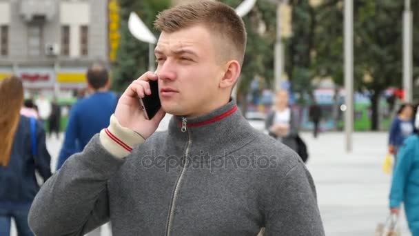 都市の広場で携帯電話で話している若いハンサムな男の肖像. — ストック動画