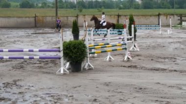 Profesyonel kadın jokey at sırtında sürmek. At kumun üzerinde çalışır ve bir engel atlar.