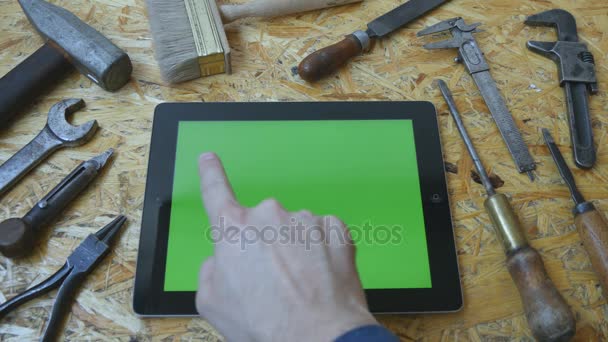 Мужская рука ремесленника с помощью планшетного ПК с зеленым экраном в мастерской. Вид сверху. Различные старинные инструменты лежат рядом — стоковое видео