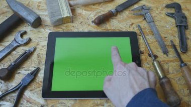 Marangozluk aletleri arka planda tutan tablet pc atölye tablo ile manzara modunda. Adam el ile yeşil ekran tablet kullanma. Üstten Görünüm