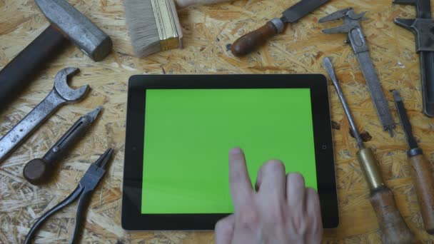 Male hand of artisan craftsman using tablet pc with green screen in workshop. Top view. Different vintage tools lie beside — Stock Video