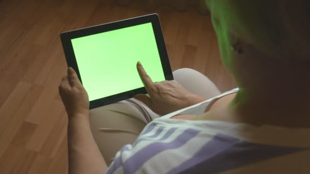 Femme âgée assise sur un canapé à la maison et utilisant une tablette numérique PC avec écran vert, vue arrière. Tablette PC dans les mains d'une femme adulte — Video