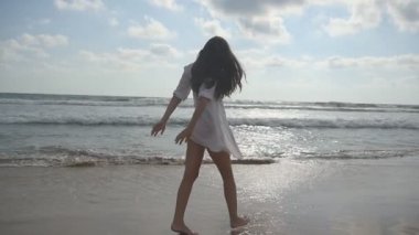 Okyanus kıyısında yürüyen ve dönen mutlu bir kadın. Genç ve güzel bir kız hayatın tadını çıkarıyor ve deniz kıyısında eğleniyor. Yaz tatili ya da tatil. Arka planda doğa manzarası. Yavaş çekim