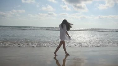 Yürüyüş ve Okyanusu yakınlarındaki sahilde oynarken mutlu bir kadın. Genç güzel kız hayattan zevk ve deniz sahilinde eğleniyor. Yaz tatili ya da tatil. Arka plan egzotik manzaraya. Ağır çekim