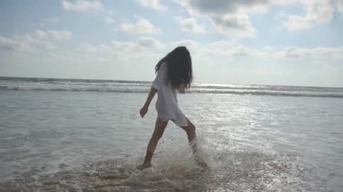 Okyanus Sahilde yürüyüş ve su püskürtme ayakları ile mutlu bir kadın. Genç güzel kız hayattan zevk ve deniz sahilinde eğleniyor. Yaz tatili. Arka plan manzara. Slowmotion