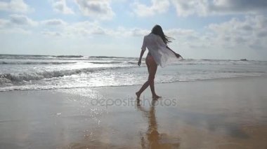 Mutlu kadın bikini ve Okyanusu yakınlarındaki Sahilde yürüyüş gömlek. Genç güzel kız hayattan zevk ve deniz sahilinde eğleniyor. Yaz tatili ya da tatil. Arka arka görüş. Ağır çekim