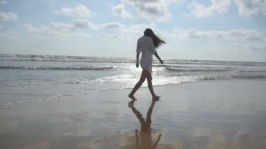 Yürüyüş ve Okyanusu yakınlarındaki sahilde oynarken mutlu bir kadın. Genç güzel kız hayattan zevk ve deniz sahilinde eğleniyor. Yaz tatili ya da tatil. Arka geri görüntülemek ağır çekim