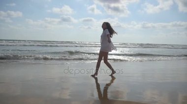 Okyanus kıyısında yürüyen ve dönen mutlu bir kadın. Genç ve güzel bir kız hayatın tadını çıkarıyor ve deniz kıyısında eğleniyor. Yaz tatili ya da tatil. Arka planda doğa manzarası. Yavaş çekim