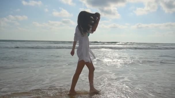 Mulher feliz andando descalça na água na praia perto do oceano. Menina bonita nova desfrutando a vida e se divertindo na praia. Férias de verão ou férias. Paisagem natural no fundo. Movimento lento — Vídeo de Stock