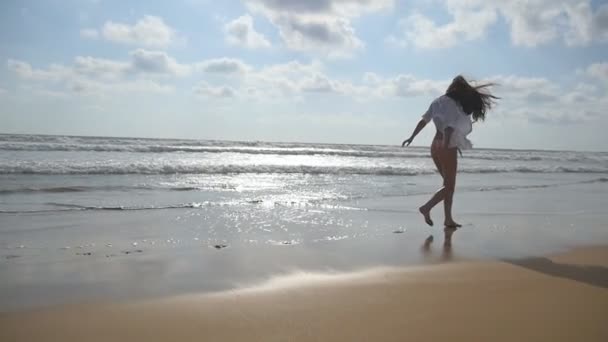 Счастливая женщина бегает или бегает по пляжу возле океана. Молодая красивая девушка наслаждается жизнью и веселится на берегу моря. Летние каникулы или каникулы. Природа на заднем плане. Медленное движение — стоковое видео