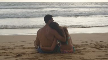 Genç romantik çift güzel günbatımı sahilde oturan ve sarılma keyif alıyor. Bir kadın ve bir adam oturuyor birlikte deniz kıyısında kum okyanus ve manzara hayran. Slowmotion yakından