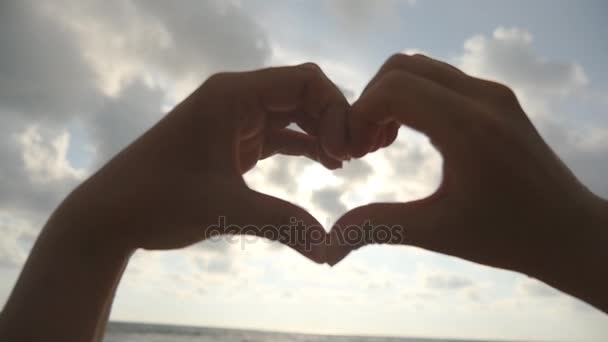 Ragazza che fa cuore con le mani sul fondo del mare con un bel tramonto dorato. Silhouette del braccio femminile a forma di cuore con alba all'interno. Concetto di vacanza. Vacanze estive sulla spiaggia. Rallentatore — Video Stock