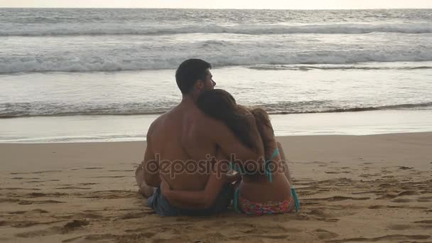 Genç romantik çift güzel günbatımı sahilde oturan ve sarılma keyif alıyor. Bir kadın ve bir adam oturuyor birlikte deniz kıyısında kum okyanus ve manzara hayran. Slowmotion yakından — Stok video