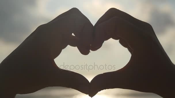 Chica haciendo corazón con sus manos sobre el fondo del mar con hermosa puesta de sol de oro. Silueta de brazo femenino en forma de corazón con salida del sol en el interior. Concepto de vacaciones. Vacaciones de verano en playa. Movimiento lento — Vídeos de Stock