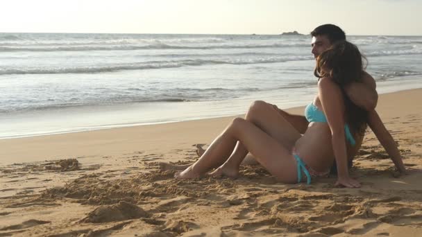 Joven pareja romántica está disfrutando de una hermosa vista sentada en la playa y abrazándose. Una mujer y un hombre se sientan juntos en la arena en la orilla del mar, admirando el océano y los paisajes. — Vídeos de Stock