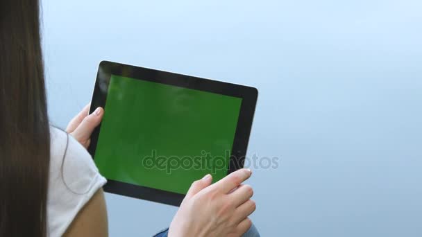 年轻的女孩坐在湖边的木码头上的绿色屏幕使用数字 tablet pc。后视图. — 图库视频影像