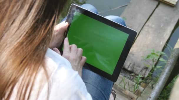 Frauenhände mit digitalem Tablet-PC mit grünem Bildschirm sitzen auf einem Holzsteg am See. — Stockvideo