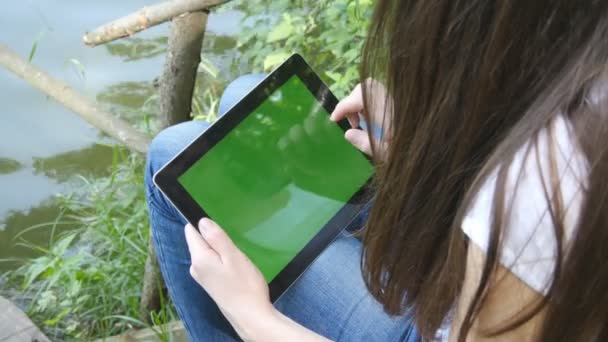 Female hands using digital tablet pc with green screen sitting on a wooden jetty by the lake. — Stock Video