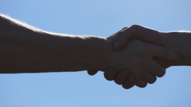 Mavi gökyüzü arka plan üzerinde iki tanınmaz kas beyaz adamın dostu el sıkışma. Erkek silah açık sallayarak. İki güçlü adam dışında firma el sıkışma sahip. Takım çalışması ve dostluk. Yakın çekim