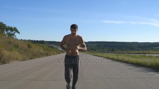 Un corredor corriendo trotando en la autopista. Deportista masculino entrenando al aire libre en verano. Joven chico musculoso fuerte haciendo ejercicio en la carretera rural durante el entrenamiento. Estilo de vida saludable activo afuera. De cerca. — Vídeos de Stock