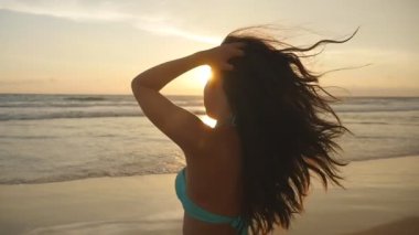 Bikini ayakta deniz günbatımı güzel genç kadın. Erkek sahilde tatil sırasında hayattan zevk. Okyanus kıyısında güneş doğarken poz uzun saçlı çekici seksi kız. Ağır çekim