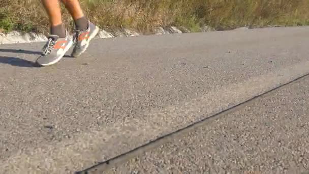 Foten av stark man kör på vägen i sommar. Manliga ben jogging under träning träning på land rutt vid solnedgången. Ung man är träning på en tom asfalt bana. Träna utomhus, närbild — Stockvideo