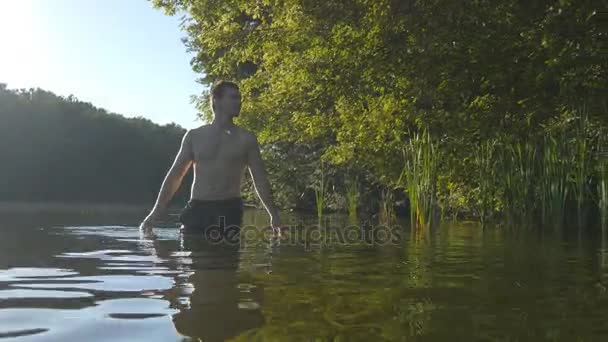 Mladý muž stál ve vodě, v létě a relaxaci. Guy odpočinek u řeky — Stock video
