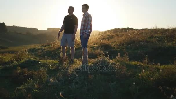 Retrato del padre con su hijo hablando al aire libre al atardecer. Dos hombres adultos están de pie sobre hierba verde en la colina y hablando entre sí. Padre e hijo pasan tiempo juntos en la naturaleza por la noche — Vídeos de Stock