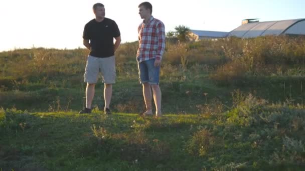 Retrato del padre con su hijo hablando al aire libre al atardecer. Dos hombres adultos están de pie sobre hierba verde en la colina y hablando entre sí. Padre e hijo pasan tiempo juntos en la naturaleza por la noche — Vídeos de Stock