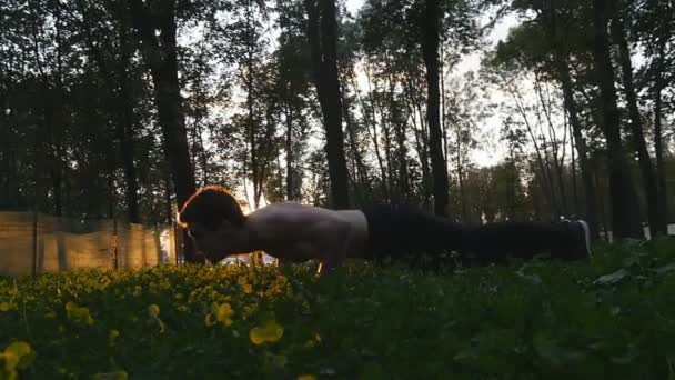 Чоловік-спортсмен робить стрибки на відкритому повітрі. Молодий чоловік тренується в міському парку на заході сонця. Впритул спортсмен тренується на вулиці з красивим схід сонця на фоні. Повільний рух . — стокове відео