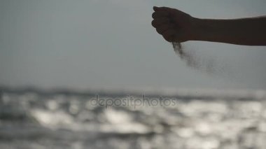 Erkek bir okyanus arka plan gün batımında onun parmaklarının arasından dökülen deniz kum el. Kol strewed veya ondan düşen kum ile genç kadın. Kum kız yumruk yoğun sis. Ağır çekim yakın çekim
