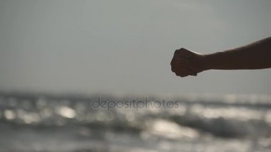 Erkek bir okyanus arka plan gün batımında onun parmaklarının arasından dökülen deniz kum el. Kol strewed veya ondan düşen kum ile genç kadın. Kum kız yumruk yoğun sis. Ağır çekim yakın çekim