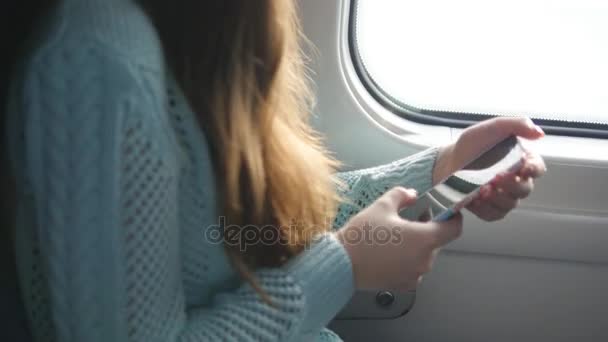 Young girl travelling in a train and using mobile phone. Beautiful woman sends a message from the smartphone. Attractive girl chatting with friends — Stock Video