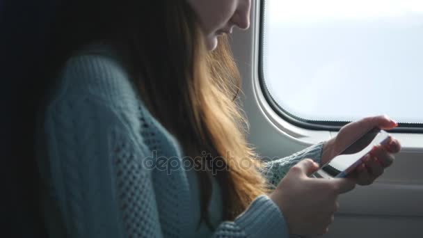 Menina viajando em um trem e usando telefone celular. Mulher bonita envia uma mensagem do smartphone. Menina atraente conversando com amigos — Vídeo de Stock