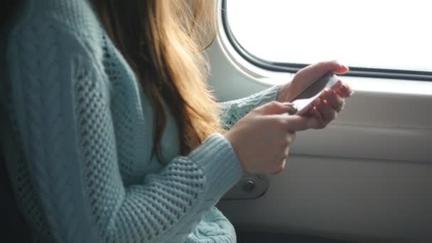 Девушка путешествует в поезде и пользуется мобильным телефоном. Красивая женщина отправляет сообщение со смартфона. Привлекательная девушка болтает с друзьями — стоковое видео