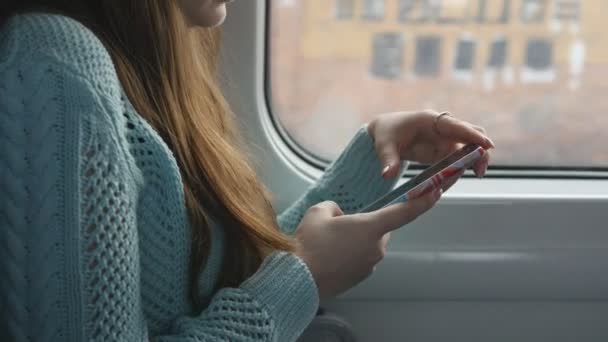 Молода дівчина подорожує потягом і використовує мобільний телефон. Красива жінка надсилає повідомлення зі смартфона. Приваблива дівчина спілкується з друзями — стокове відео