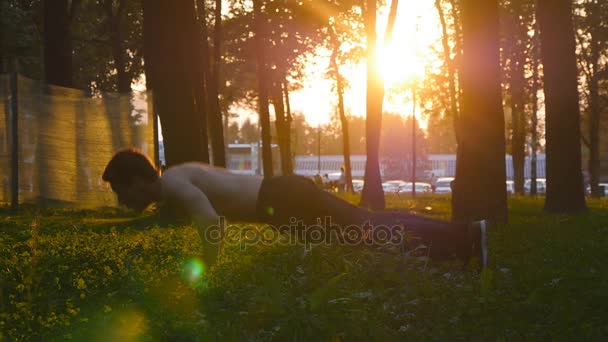 Hombre atleta haciendo flexiones con saltar al aire libre. Un joven entrena en el parque de la ciudad al atardecer. Primer plano de entrenamiento de deportista afuera con hermoso amanecer en el fondo. Movimiento lento — Vídeo de stock