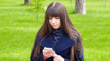 Güzel kadın hücre smartphone açık havada park - ayrıntı kullanır. Genç çekici mutlu kız bir şehir parkında rahatlatır ve bir cep telefonu kullanır. O çok mutlu ve memnun görünüyor