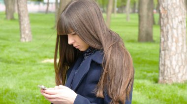 Parkta - ayrıntı için bekleyen güzel bir kadın bul. O etrafa ve mibile akıllı telefon kullanır.